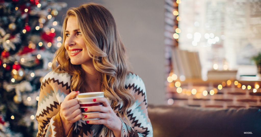 Woman indoors in front of Christmas tree with mug