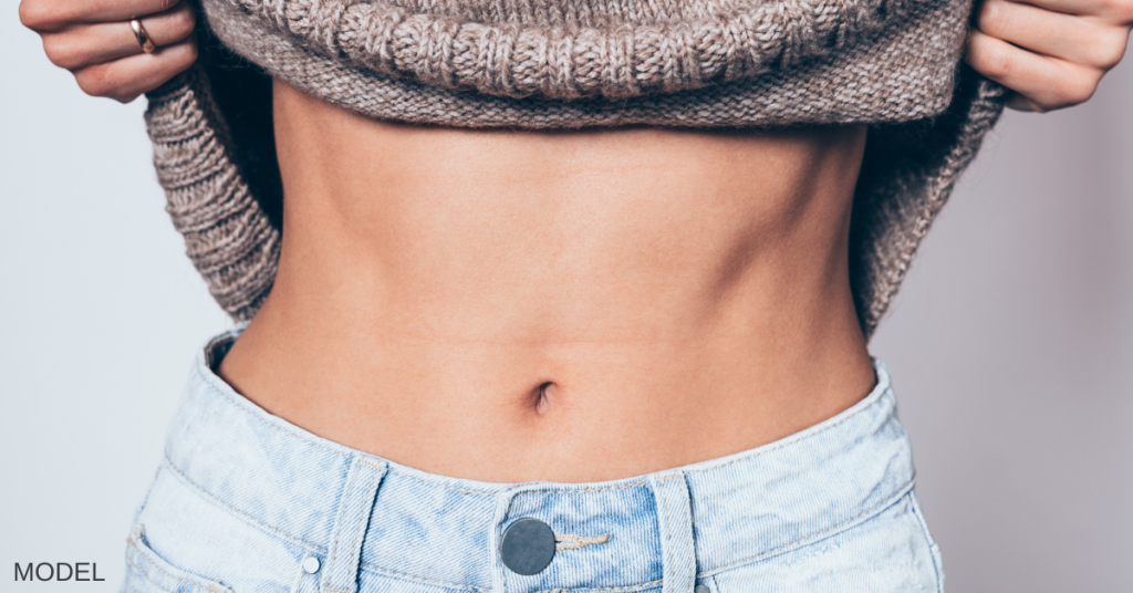 Woman wearing a sweater and jeans and lifting her sweater to expose her stomach (model)