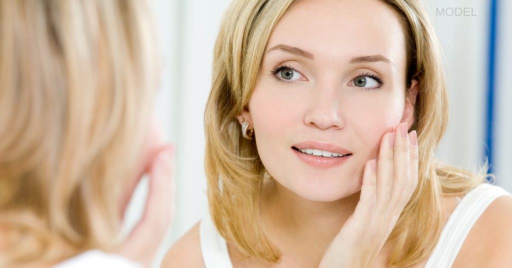 Woman looking in mirror and touching her face (MODEL)