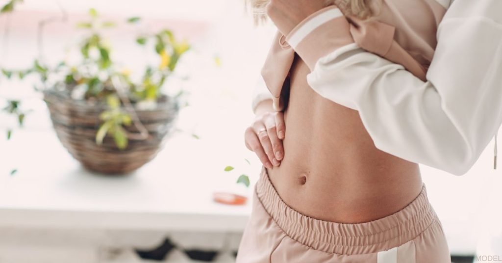 A physically fit woman is lifting her sweatshirt to show her belly. (MODEL)