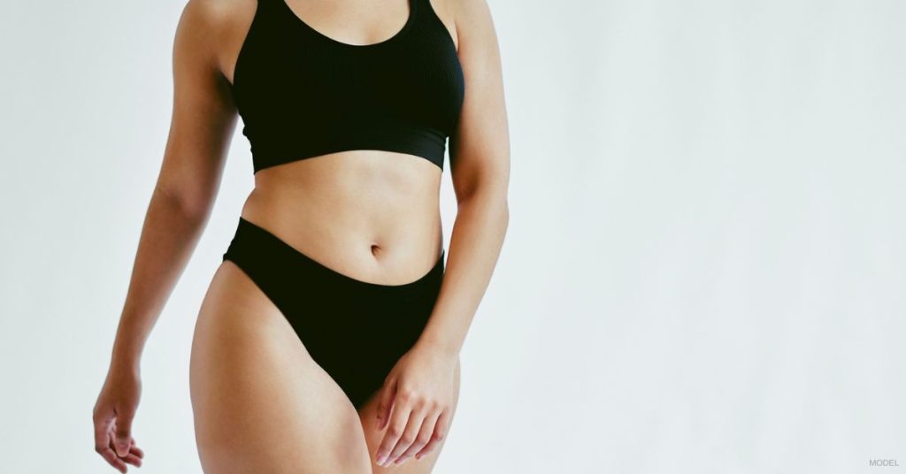 A woman in black undergarments in front of a white background. (Model)