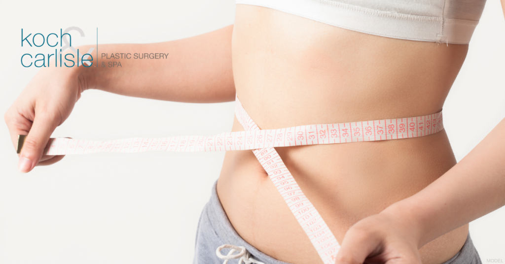 A woman wrapping a tape measure around their waist to measure weight loss (model). Koch Carlisle Plastic Surgery & Spa logo.